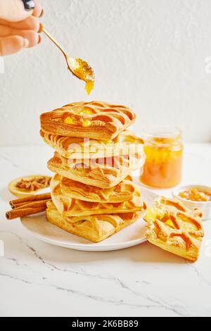 La mano della donna mette un cucchiaio di marmellata di agrumi su una pila di pasta sfoglia Foto Stock