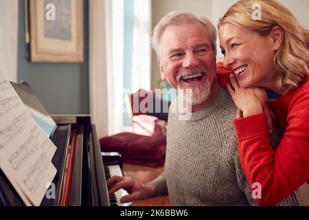 Coppia sorridente anziano a casa godendo imparare a suonare il piano Foto Stock