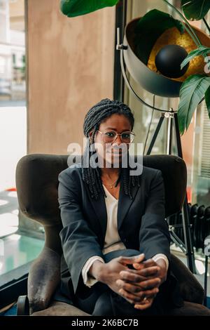 Ritratto di una giovane donna d'affari che indossa occhiali seduti sulla sedia nella sala dell'hotel Foto Stock
