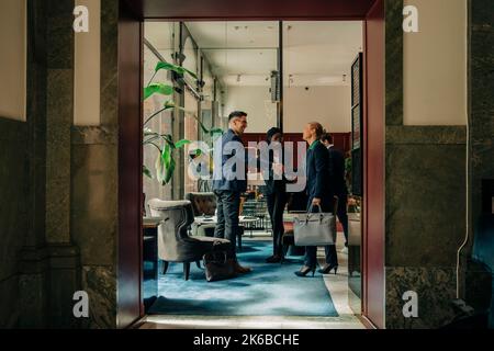 Un'intera gamma di professionisti maschili e femminili che fanno una stretta di mano mentre sono in piedi da un collega nella sala dell'hotel Foto Stock