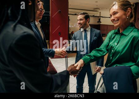 Sorridenti imprenditori maschili e femminili che scuotono le mani nella sala dell'hotel Foto Stock