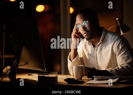 Im preoccupato che questa potrebbe essere la decisione sbagliata... un giovane uomo d'affari che guarda preoccupato mentre beve il caffè e lavorando su un computer in un ufficio a. Foto Stock