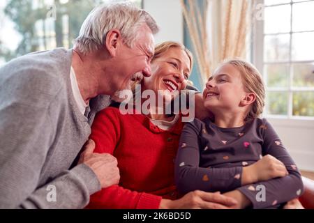 I nonni amorevoli abbracciano la nipote seduta sul divano a casa insieme Foto Stock