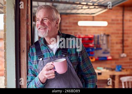 Ritratto di Senior Male indossare tute in officina Garage con bevanda calda Foto Stock