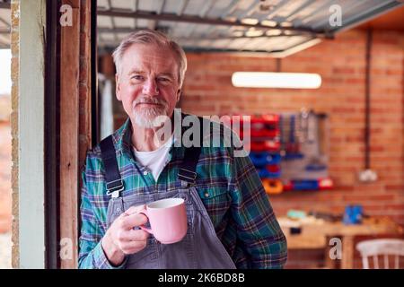 Ritratto di Senior Male indossare tute in officina Garage con bevanda calda Foto Stock