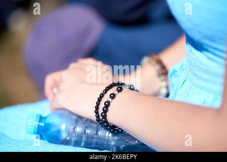 Rosario in forma di bracciale con perle nere e croce d'argento sul polso di una ragazza in abito blu. Primo piano. Foto Stock