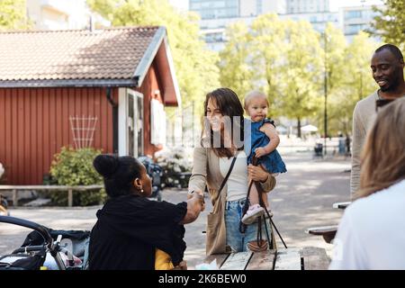 Donna sorridente che porta figlia facendo stretta di mano con l'amico femmina al parco Foto Stock