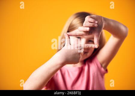 Studio Ritratto di ragazza sorridente facendo forma di cornice con le mani contro sfondo giallo Foto Stock