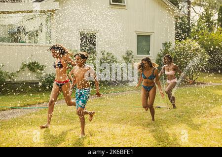 Una famiglia allegra che passa attraverso un irrigatore nel cortile posteriore Foto Stock