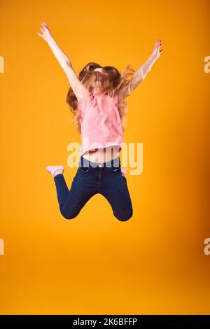 Studio Shot di energica ragazza in aria con braccia allungate contro sfondo giallo Foto Stock