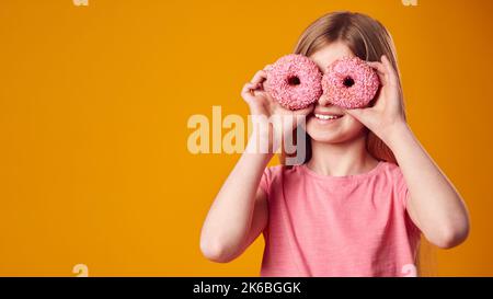 Studio Ritratto di ragazza che tiene due ciambelle davanti agli occhi contro sfondo giallo Foto Stock