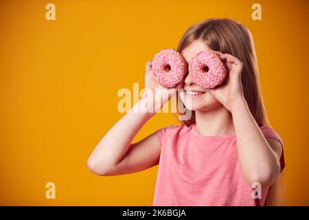 Studio Ritratto di ragazza che tiene due ciambelle davanti agli occhi contro sfondo giallo Foto Stock
