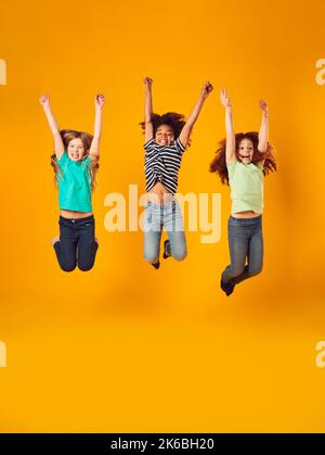 Studio Shot di bambini energici che saltano in aria con le braccia distese su sfondo giallo Foto Stock