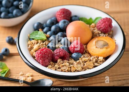 Granola croccante al miele di avena con frutti di bosco e frutti in ciotola su sfondo tavolo di legno, vista primo piano Foto Stock