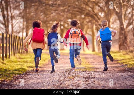 Vista posteriore dei bambini con gli zaini scolastici all'aperto che corrono lungo il percorso della campagna Foto Stock