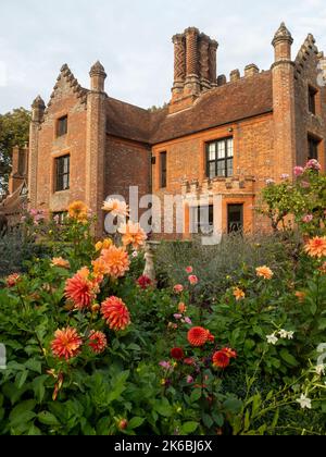 Chenies Manor e giardino circondato da colorate dahlias nel mese di ottobre.Dahlia 'Grande Ercole' fiori di bronzo arancione sopra il resto. Foto Stock