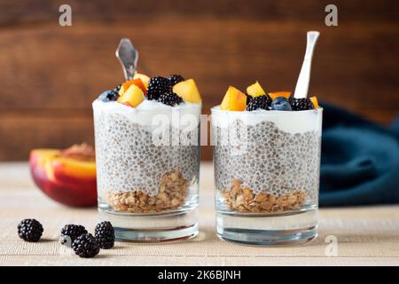 Budino di Chia in vaso di vetro con frutti di bosco e granola. Sfondo in legno con spazio copia Foto Stock