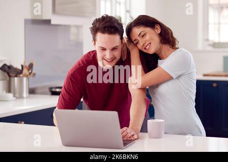 Amare la coppia Transgender a casa insieme guardando il notebook sul bancone della cucina Foto Stock