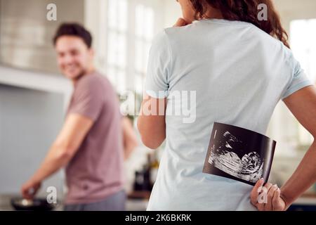 Coppia incinta Transgender a casa in cucina con Donna uomo sorprendente con scansione ecografica del bambino Foto Stock