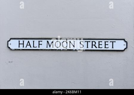 Primo piano della targa del nome della strada, Half Moon Street, su un vecchio sfondo dipinto di grigio. Il segno di testo vintage è scritto in nero su un metallo bianco Foto Stock