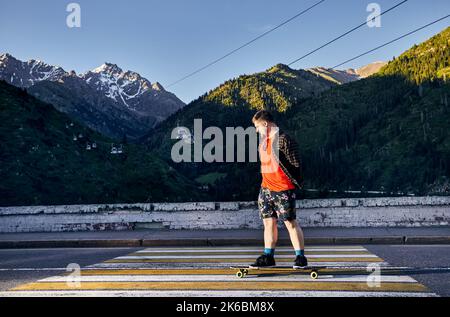 Uomo barbuto Skater che viaggia sulla strada di montagna sul suo longboard a Medeo Dum Almaty, Kazakhstan Foto Stock