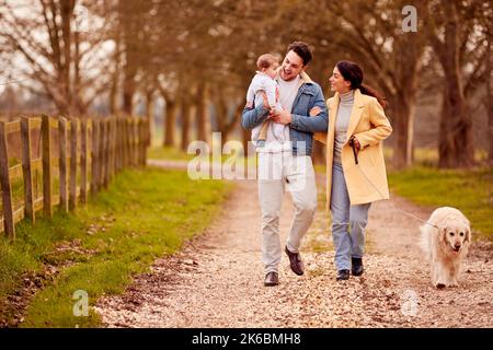 Famiglia transgender con Baby and PET Dog che si gode una passeggiata nella campagna autunnale o invernale Foto Stock