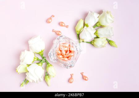 Capsule in oro rosa con olio cosmetico per il viso in vaso di vetro con composizione floreale di eustoma su sfondo rosa. Pacchetto uso singolo. Cosmetici da viaggio. C Foto Stock