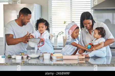 Tutti possono aiutare in cucina: Una coppia che cuoce a casa con i loro tre figli. Foto Stock