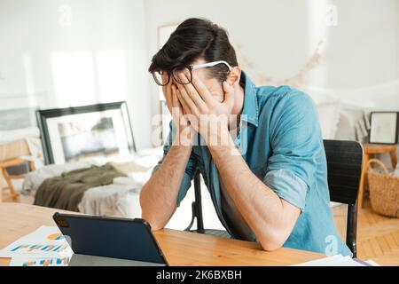Rovesciato giovane uomo caucasico pagare bollette sensazione di stress a causa di problemi finanziari. Il freelance ha perso i suoi soldi e non può pagare le sue tasse. Financi Foto Stock