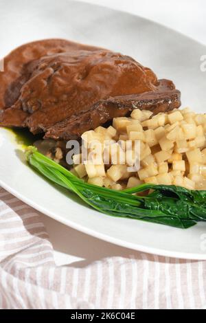 Guance di manzo brasate tradizionali tedesche in salsa di vino rosso bruno con risotto al sedano su sfondo bianco per il menu del ristorante. Foto Stock