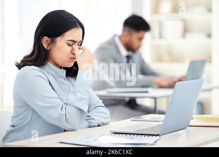 Non riesco a elaborare nulla con questo mal di testa. Una giovane donna d'affari che guarda stressato mentre lavora su un portatile in un ufficio. Foto Stock