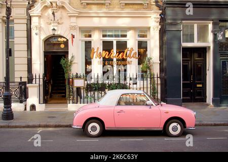 Una bella foto di una Nissan Figaro rosa in strada a Henrietta St, Londra Foto Stock