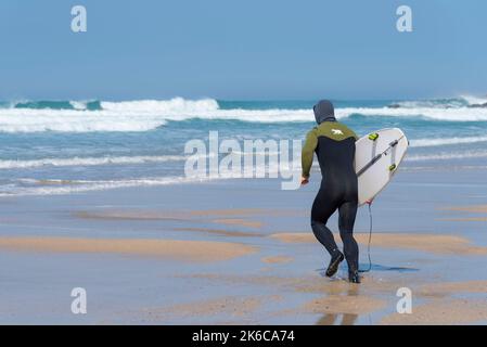 Un appassionato surfista che trasporta una tavola da surf e corre verso il mare a Fistral a Newquay in Cornovaglia nel Regno Unito. Foto Stock