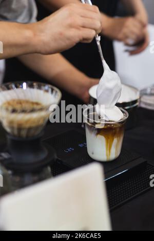 Barista che prepara caffè latte ghiacciato con panna montata a mano nel bar. Foto Stock