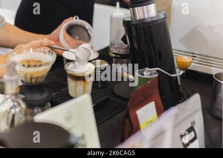 Barista che prepara caffè latte ghiacciato con panna montata a mano nel bar. Foto Stock