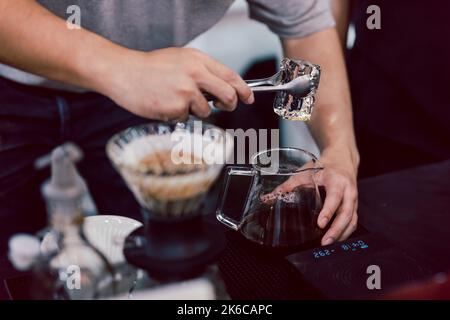 Barista preparare il caffè ghiacciato mettendo un ghiaccio in un bicchiere di vetro con caffè nero appena preparato. Foto Stock