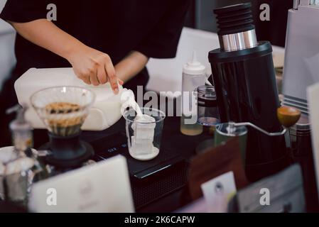 Barista donna che prepara il latte di caffè versa il latte in un bicchiere. Foto Stock