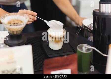 Barista che prepara caffè latte ghiacciato con panna montata a mano nel bar. Foto Stock