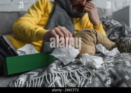 vista parziale dell'uomo malato sdraiato sul divano con coperta calda e tovagliolo di carta, immagine di scorta Foto Stock