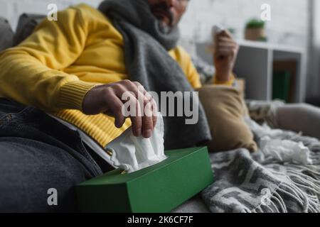 vista parziale del malato sdraiato sul divano e prendendo tovagliolo di carta dalla confezione, immagine di scorta Foto Stock