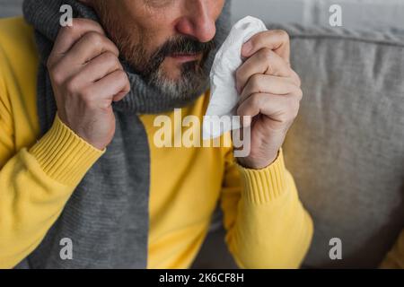 vista parziale dell'uomo malato in tovagliolo di carta con sciarpa calda, immagine di scorta Foto Stock