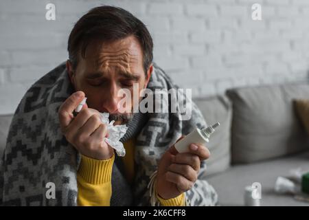 uomo malato con occhi chiusi che soffre di naso che cola e tenendo spray nasale con tovagliolo di carta, immagine stock Foto Stock