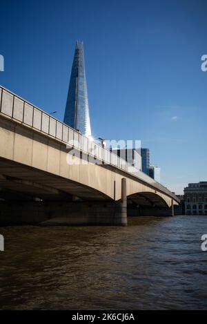 London Bridge e il Tamigi in primo piano immersi nel sole con lo Shard, con la luce che si riflette in un paesaggio verticale londinese. Foto Stock