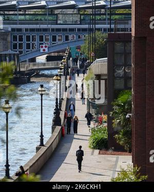 Una vista che guarda dal Millennium Bridge verso il Blackfriars Railway Bridge lungo St Pauls Walk con persone che camminano al sole del pomeriggio. Foto Stock