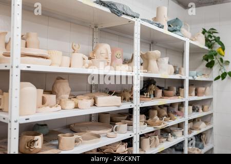 diverse sculture in argilla vicino a tazze e ciotole su scaffali di negozio di ceramica, immagine stock Foto Stock