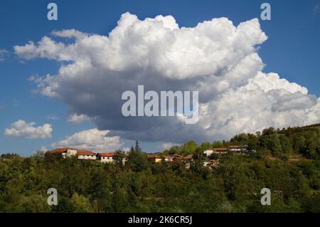 Nuvole di Cumulus, grandi nuvole bianche, sopra un villaggio su una collina boscosa in Toscana, Italia Foto Stock