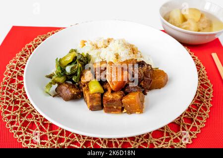 Cubo caramellato di pancia di maiale arrosto, cavolo stufato e kohlrabi, riso su piatto, bastone su tela rossa da tavolo e cerchio di bambù pad, composta. Foto Stock