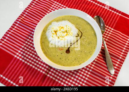 Zuppa di broccoli con semi di sesamo, olio di cumino nero e crema su un panno da tavolo rosso a scacchi su fondo bianco. Foto Stock