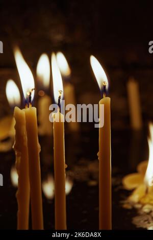 Candele di cera di preghiera illuminate usate per una preghiera cristiana, con fiamma intensa e cera fusa sulla superficie di acqua scura all'interno di una chiesa. Foto Stock