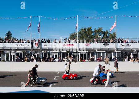 I genitori e i loro figli spingono le loro auto a pedali Austin J40 all'inizio della gara di Settrington Cup per bambini, BARC Revival Meeting, Goodwood, UK Foto Stock